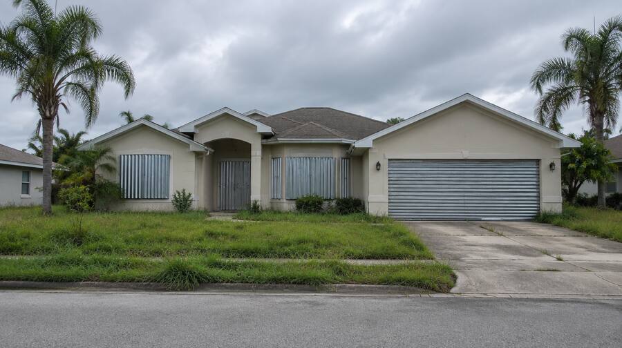Vacant Florida house with closed hurricane shutters under a grey sky.